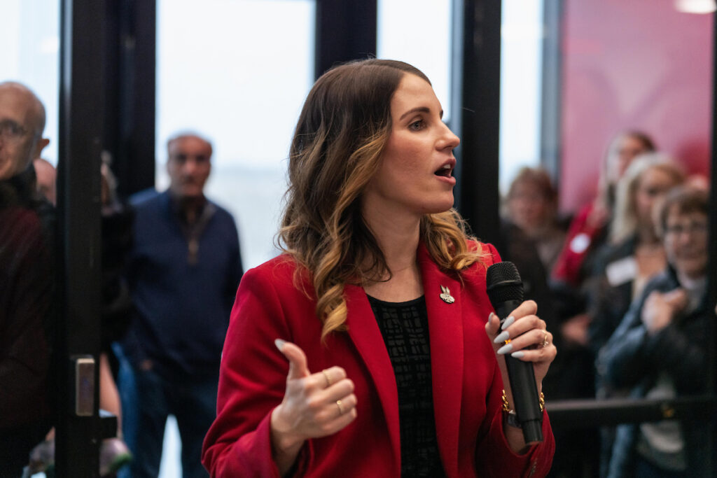 A photograph of Alissa Matt, Assistant Vice President for External Relations at the University of South Dakota, speaking to attendees at the USD Discovery District Grand Opening while holding a microphone.A photograph of Alissa Matt, Assistant Vice President for External Relations at the University of South Dakota, speaking to attendees at the USD Discovery District Grand Opening while holding a microphone.
