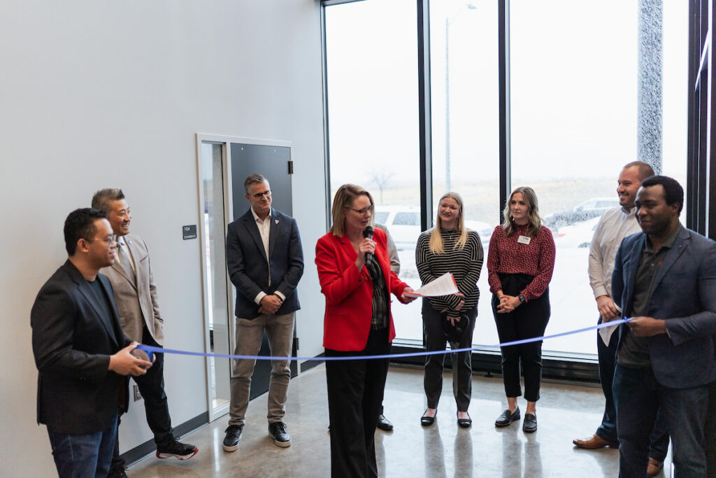 President Sheila Gestring speaks and prepares to cut the ribbon during the USD Discovery District Grand Opening, surrounded by campus and community leaders.