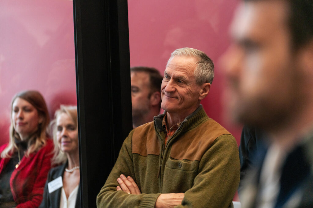 Former Governor Dennis Daugaard standing with arms crossed, listening to program remarks at the USD Discovery District Grand Opening.