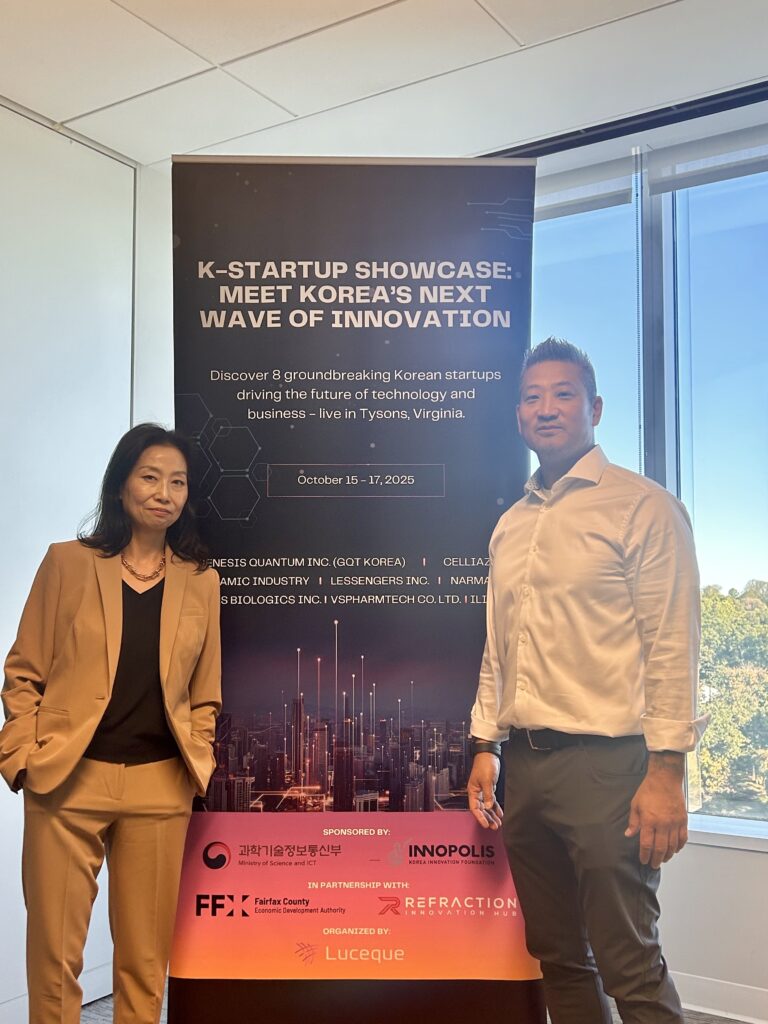 Julie Koo of Luceque Global and Ryan Oines stand beside the K-Startup Showcase banner inside a conference room in Tysons, Virginia.