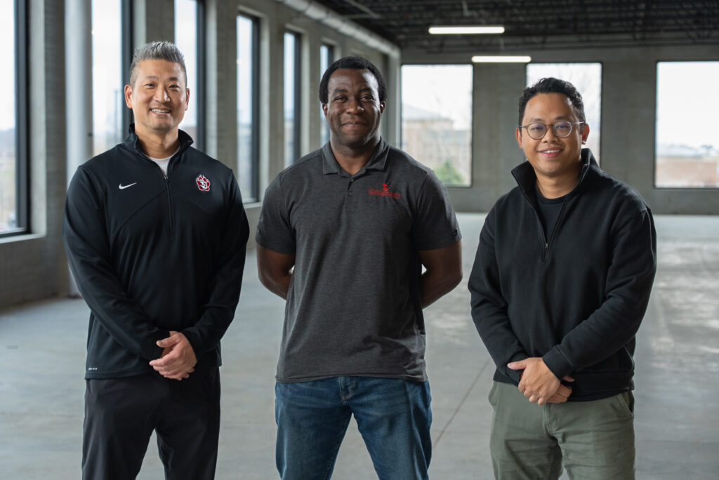 Marc standing with two colleagues inside an industrial commercial space with large windows and exposed steel beams.